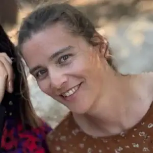 Vrouw met lichtbruin haar en blauwe ogen lachend op natuurlijke achtergrond.